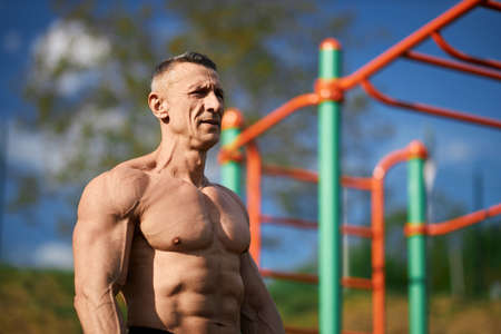 Fitness caucasian man with muscular bare torso standing on sports ground and looking aside. Strong...