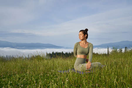 Healthy fit lady in sport clothes sitting on yoga mat and doing fitness exercises outdoors. Concept...