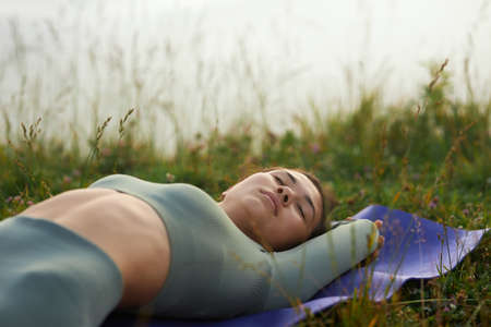 Side view of female in green wear sleeping outdoors after doing yoga exercises. Crop of woman...