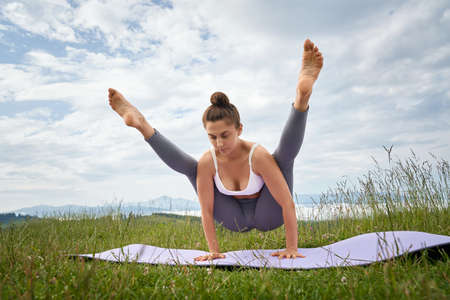 Brunette woman holding balance on hands on yoga mat, looking down. Pretty serious female standing in...