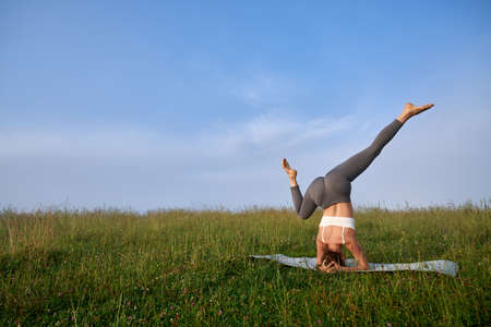Strong young woman in sport outfit practicing headstand position among summer mountains. Active...