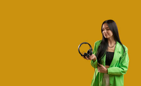 Front view of fashionable girl standing, holding earphones, smiling, Pretty brunette young woman...