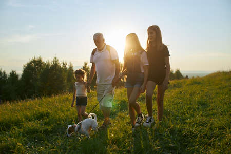 Front view of old man with three girls and dog going forward in hills. Male with gray hair and beard...
