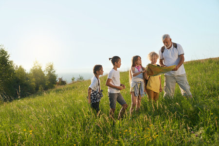 Front view of old teacher showing map to four kids in hills. Old man with gray hair looking for a...