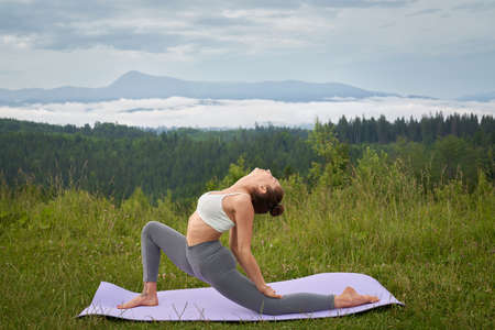 Athletic woman dressed in sport clothes doing flexible exercises on yoga mat during active workout...