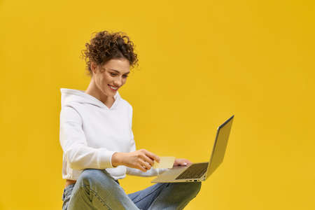 Pretty girl using laptop to make payment online in studio. Front view of smiling woman shopping...
