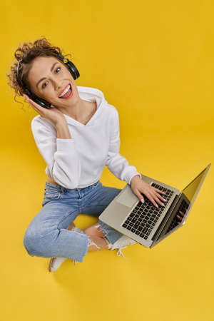 Pretty caucasian woman listening to music on laptop in studio. Above view of young girl in hoodie...