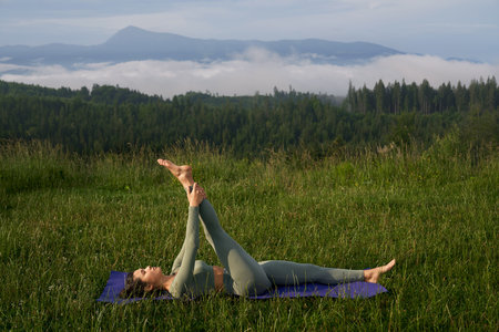 Young sporty woman enjoying yoga practice among green summer mountains. Balance between body and...