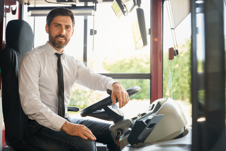Elegant male driver smiling at camera, while sitting behind steering wheel in bus. Low angle view of...