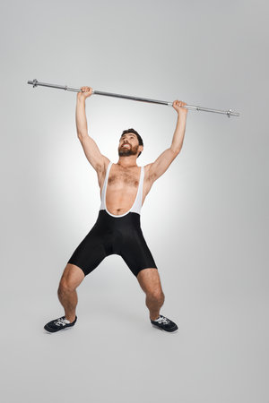 Muscular man in sportswear lifting unweighted barbell in studio. Full length of male powerlifter with clasped teeth exercising, isolated on white background. Concept of weightlifting, sport activity.の写真素材