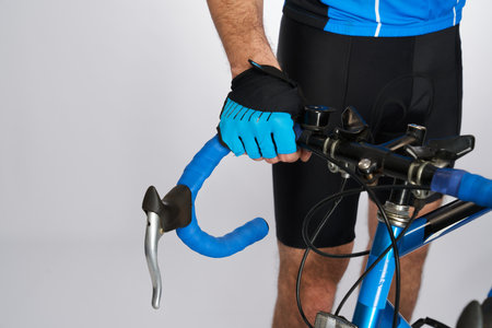 Detail of handlebar of modern blue racing bicycle holding by male athlete. Crop view of unrecognizable cyclist in black bib shorts and gloves carrying bike, isolated on grey. Cycling, sport concept.の写真素材