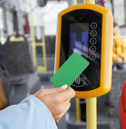 Crop of female hand holding green paying card in front of validator while boarding in public vehicle. Close up view of hand using terminal in transport. Concept of modern electronics devices.の写真素材