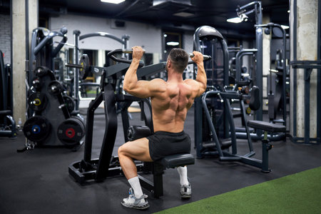 Attractive muscular man doing exercise with training apparatus in sports gym. Back view of strong unrecognizable male athlete with bare torso, building muscles indoors. Sport, bodybuilding concept.の写真素材