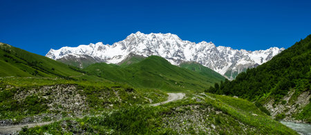 Panoramic view of green mountain valley on the foreground and steep alpine ridge on the backgroundの写真素材