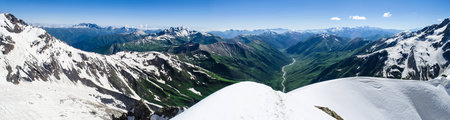 Panoramic view of alpine mountain environment with steep peaks and mountain river in the valley