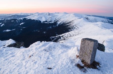 Sunset view of snowy mountain ridge with a former Polish-Czechoslovak border column in the foregroundの写真素材