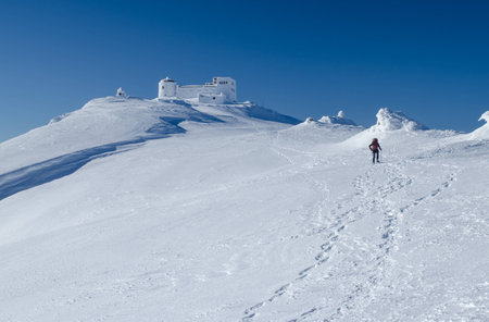 Winter picture of a hiker walking towards the abandoned observatory atop the mountain Pip Ivan in Ukrainian Carpathians. It goes through the process of reconstruction nowの写真素材