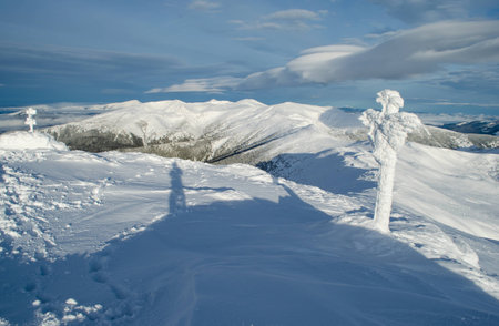 Winter mountain landscape with a shadow of the photographer and a cross covered with rimeの写真素材