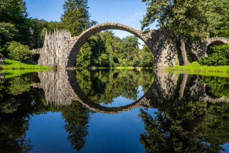 a semi-circular arched bridge made of basalt over a pond reflected in the waterの写真素材