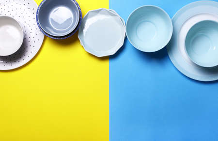 Empty ceramic tableware. Ceramic plates on yellow and blue background. Overview empty food table with tableware. Set of different modern white and blue plates and bowls.Top view, flat lay.Copy space for textの写真素材