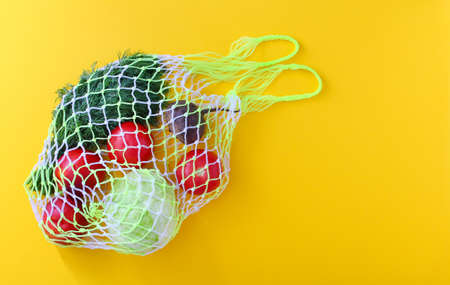 Reusable white shopping mesh bag with fruits and vegetables:tomatoes, cabbage, beetroot, dill, peaches. Zero waste concept, yellow background, copy space, close up.の写真素材