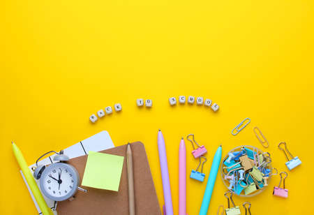 Flat lay composition of notebook, pencil,pens,binders, alarm clock.Copy space,yellow background.Top...