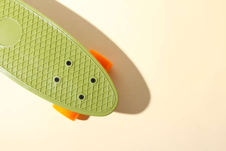 Close up of green skateboard with orange wheels on beige background. Plastic mini cruiser board....