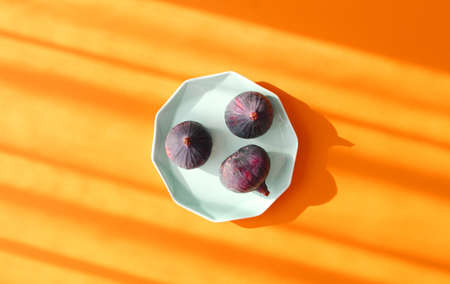 Top view of three ripe purple figs on blue plate.Healthy fruits. Flat lay,orange background.の写真素材
