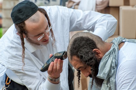 A young Hasid hairdresser mows the street another Hasid. Uman, Ukraine - October 2, 2016: Every year, thousands of Orthodox Bratslav Hasidic Jews from different countries gather in Uman to mark Rosh Hashanah, Jewish New Year, near the tomb of Rabbi Nachmaのeditorial素材