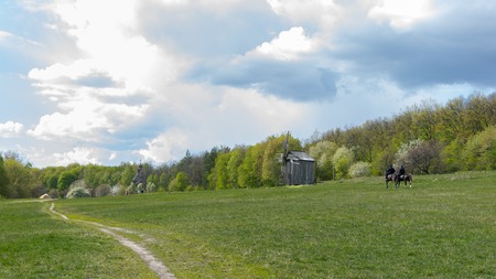 National Museum Pirogovo in the outdoors near Kiev. Ancient traditional wooden windmill and church, beautiful spring rural landscape with horsemen.のeditorial素材