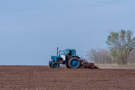 An old tractor in the field plows the land. Spring landscape of a countryside, a farm.の写真素材
