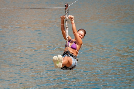 Ukraine, Migea - July 30, 2017: Zipline. The woman in the equipment slides on a steel cable. Trolley Track Over the lake. Extreme and active rest.のeditorial素材