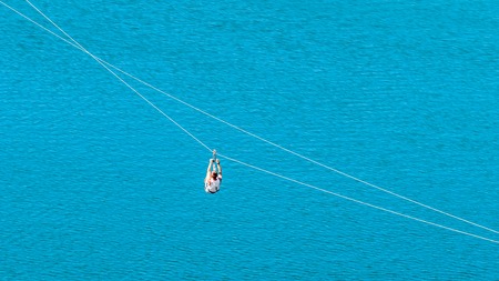 Zipline. The woman in the equipment slides on a steel cable. Trolley Track Over the lake. Extreme and active rest.の写真素材