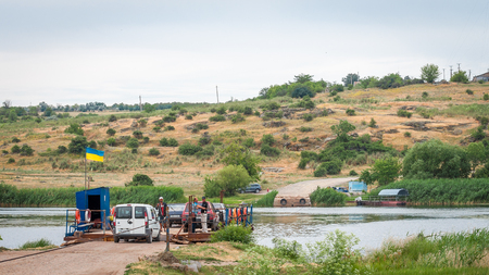 Ukraine, Southern Bug River - 18 June 2017: Ferry crossing. The ferry moves with the help of a man's muscular strength. Repels from the steel cable. Such a ferry is unique in Ukraine.のeditorial素材