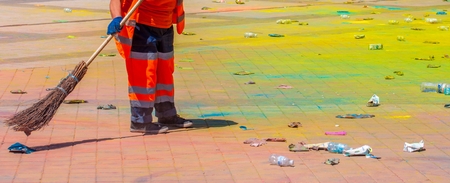 Holi's holiday is over. A lot of trash. The worker clears the territory of it rubbish and scattered paintsの写真素材