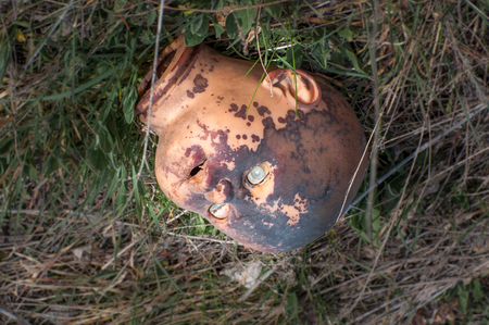 Creepy old doll head. Broken abandoned damaged scary toy in a garbage dump close-up. In the toy, the eye and mouth are damaged. The concept of fear, horror, crime. Very scary.の写真素材