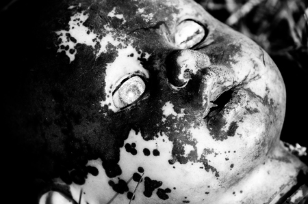Creepy old doll head. Broken abandoned damaged scary toy in a garbage dump close-up. In the toy, the eye and mouth are damaged. The concept of fear, horror, crime. Very scary.の写真素材