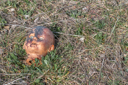 Creepy old doll head. Broken abandoned damaged scary toy in a garbage dump close-up. In the toy, the eye and mouth are damaged. The concept of fear, horror, crime. Very scary.