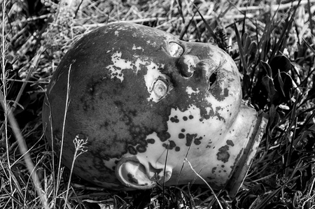 Creepy old doll head. Broken abandoned damaged scary toy in a garbage dump close-up. In the toy, the eye and mouth are damaged. The concept of fear, horror, crime. Very scary.の写真素材