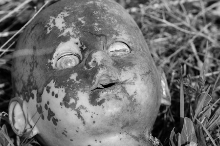 Creepy old doll head. Broken abandoned damaged scary toy in a garbage dump close-up. In the toy, the eye and mouth are damaged. The concept of fear, horror, crime. Very scary.の写真素材