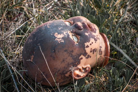 Creepy old doll head. Broken abandoned damaged scary toy in a garbage dump close-up. In the toy, the eye and mouth are damaged. The concept of fear, horror, crime. Very scary.の写真素材
