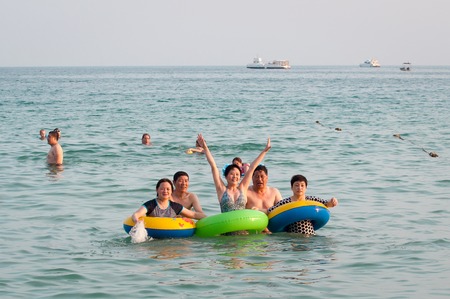 Hainan, China - May 16, 2019: A cheerful group of unidentified Chinese people are relaxing in the water on the beach of Dudonghai. The Chinese do not swim well, so they often go to sea with lifebuoysのeditorial素材