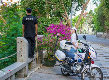 Hainan, Sanya, China - May 16, 2019. In a place where monkeys appear on the road and interfere with the movement, a policeman on a motorcycle periodically arrives and pushes them away with a stickのeditorial素材