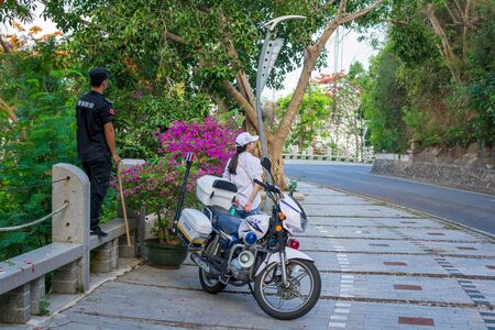 Hainan, Sanya, China - May 16, 2019. In a place where monkeys appear on the road and interfere with the movement, a policeman on a motorcycle periodically arrives and pushes them away with a stickのeditorial素材