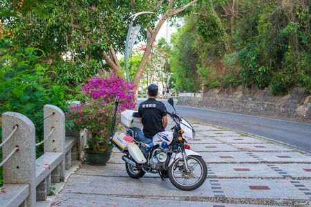 Hainan, Sanya, China - May 16, 2019. In a place where monkeys appear on the road and interfere with the movement, a policeman on a motorcycle periodically arrives and pushes them away with a stickのeditorial素材