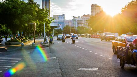 China, Hainan, Sanya - May 13, 2019: Road traffic on the background of the setting sun. Electric scooters - environmentally friendly transport. Glare on the photo, patch of reflected light, glitchのeditorial素材