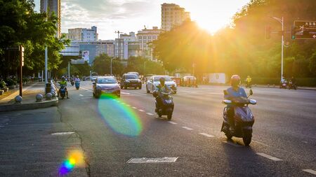 China, Hainan, Sanya - May 13, 2019: Road traffic on the background of the setting sun. Electric scooters - environmentally friendly transport. Glare on the photo, patch of reflected light, glitchのeditorial素材