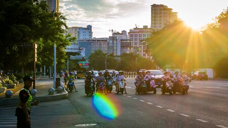 China, Hainan, Sanya - May 13, 2019: Road traffic on the background of the setting sun. Electric scooters - environmentally friendly transport. Glare on the photo, patch of reflected light, glitchのeditorial素材