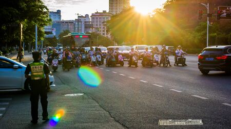China, Hainan, Sanya - May 13, 2019: Road traffic on the background of the setting sun. Electric scooters - environmentally friendly transport. Glare on the photo, patch of reflected light, glitchのeditorial素材
