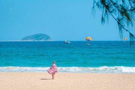 Beautiful clean beach. A young woman walks along the sandy seashore. Parasailing - a person is towed on a boat.のeditorial素材